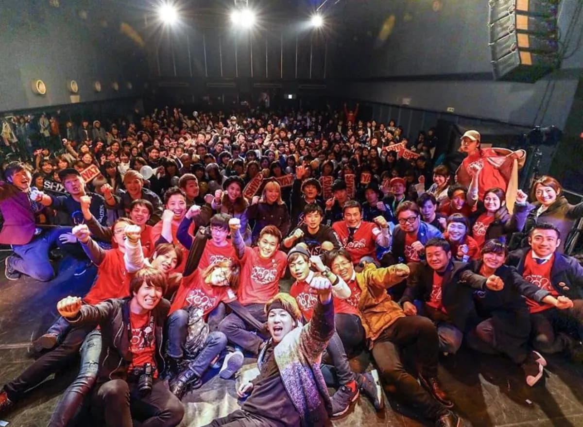 赤いTシャツのメンバーと観客が拳を上げる集合写真